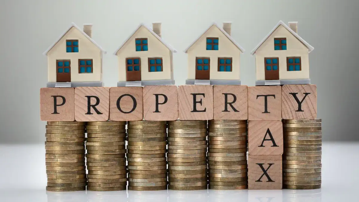 stacks of coins and wooden blocks spelling property tax on grey background