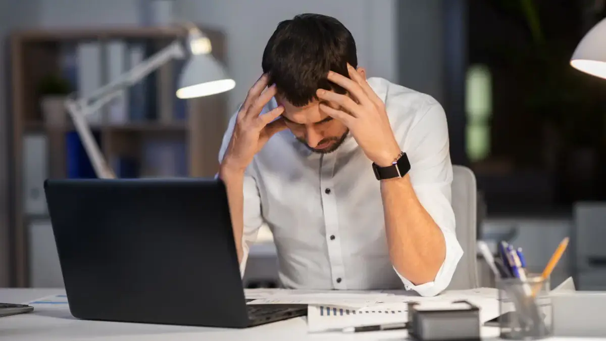 a person is sitting at their desk with their head in their hands