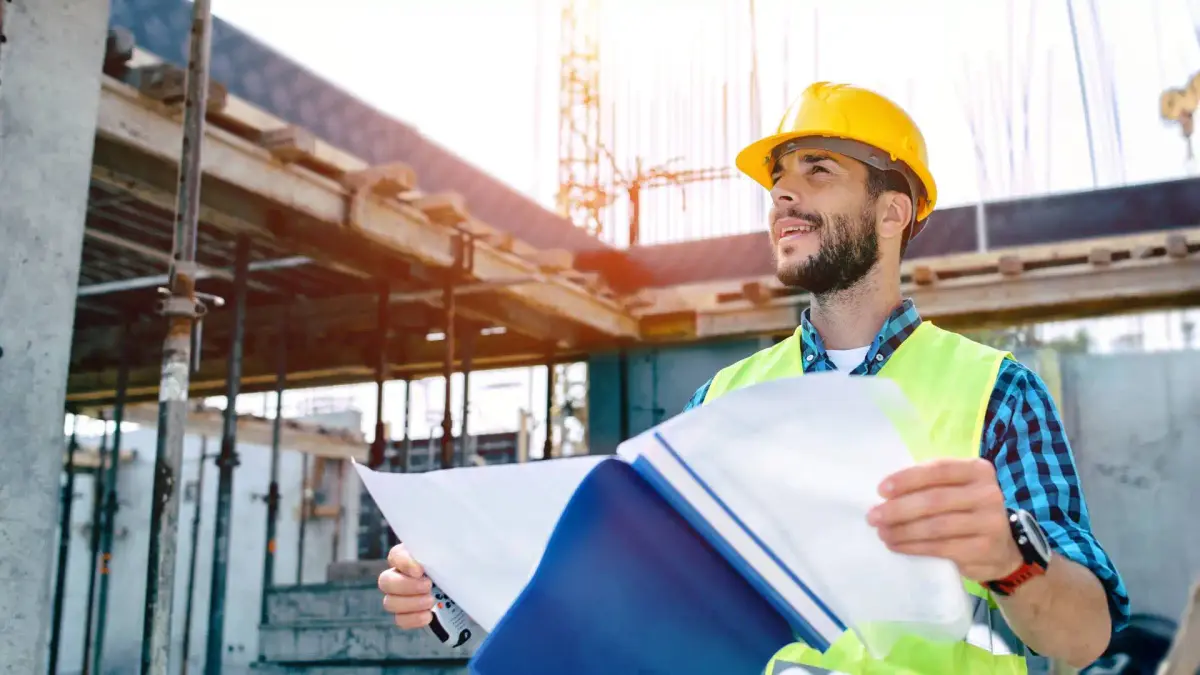 A person in a hard hat and safety vest is standing in front of a construction site