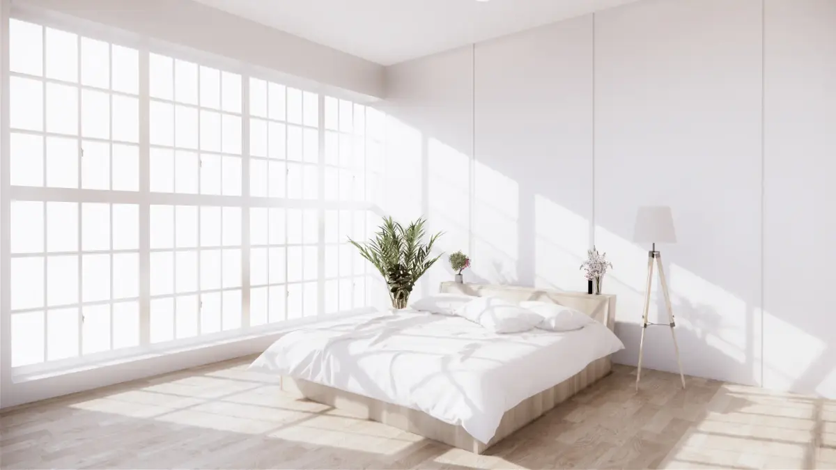 a clean white bedroom with large windows and natural sunlight coming in.